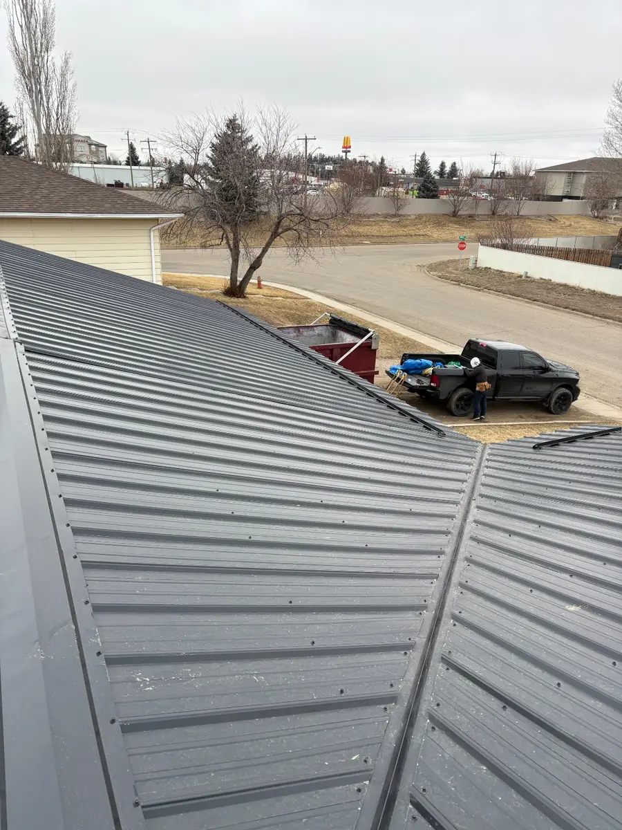 Two metal roof slopes meeting at a valley, tear-off bin and truck below