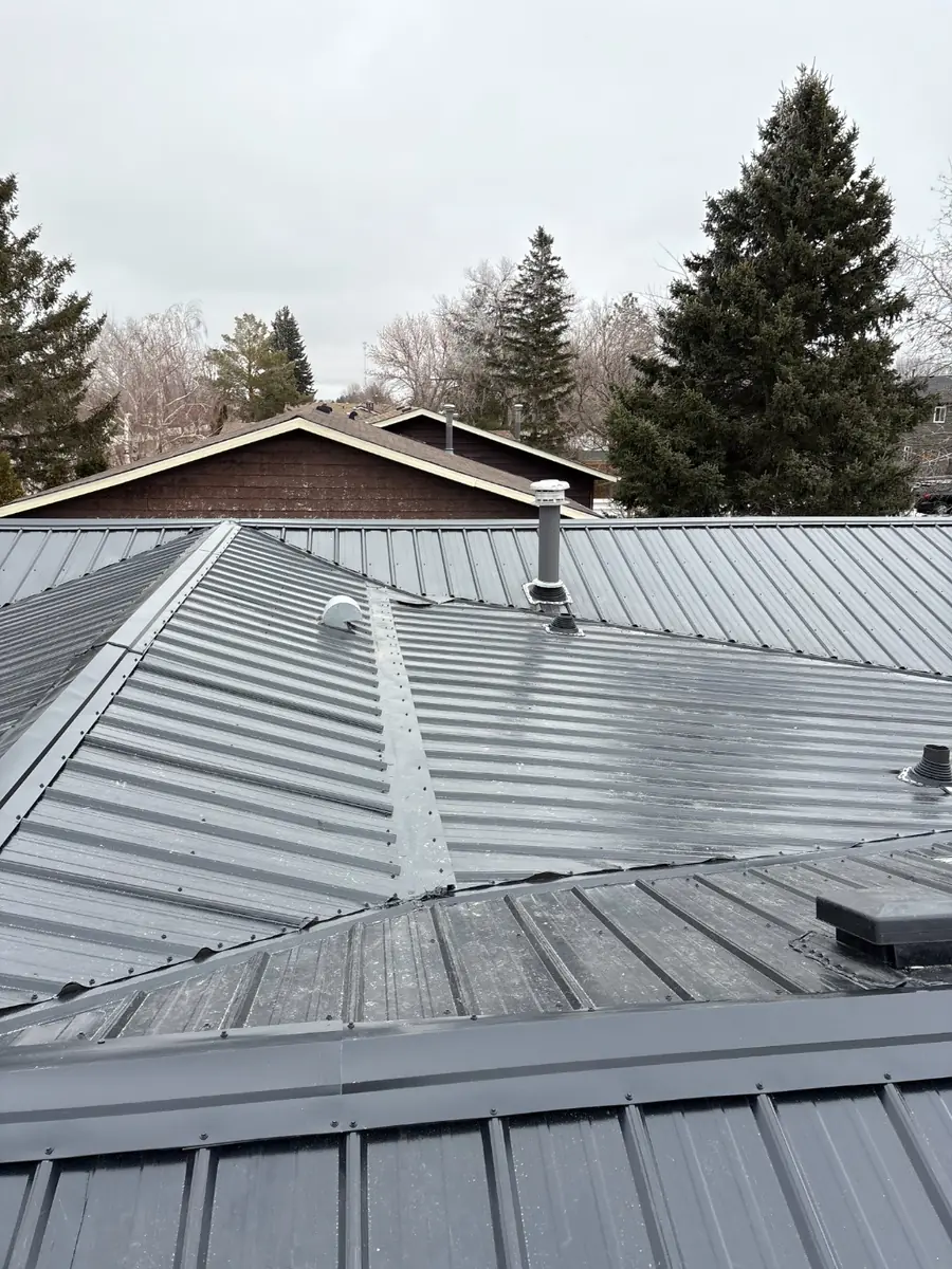 Close view of ribbed metal roof panels, ridge cap and vent boot